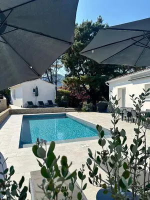 a swimming pool with an umbrella next to a house at Appartement avec terrasse privée et piscine in Sarrola-Carcopino