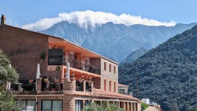 a building with a balcony with mountains in the background at Grand T2 duplex, terrasse et jardin in Porto Ota