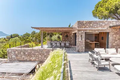 a stone house with a wooden deck with furniture at Villa Bonanza Di Cala Rossa in Lecci