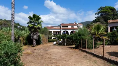 a large white house with a fence and palm trees at Casa l'Ascosu 2 in Coggia