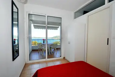 a bedroom with a red bed and a table and a balcony at Résidence Ellada 3 Appartement 12 in Cargèse