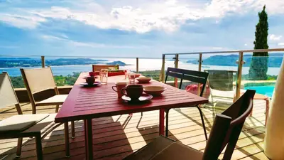 a wooden table on a balcony with a view of the water at Villa Panorama Porto-Vecchio in Porto-Vecchio