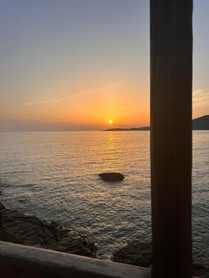 a sunset over the ocean with a rock in the water at Bleu Corse, entre mer et soleil in Ajaccio