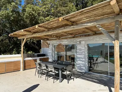 a patio with a table and chairs under a wooden pergola at Villa 8 pers vue180 golfe de Porto Vecchio in Porto-Vecchio
