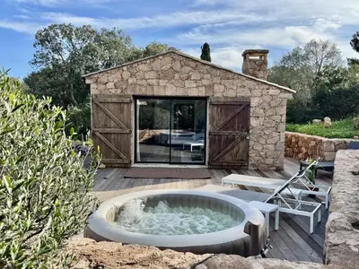 a hot tub on a deck with a building at Casetta di Asciaghju, suite avec jacuzzi privé et accès direct aux plages in Porto-Vecchio