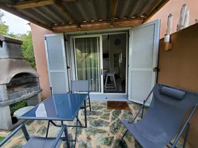 a patio with a table and chairs and a fireplace at Mini villa 200 mètres de la plage de Santa Guilia in Porto-Vecchio