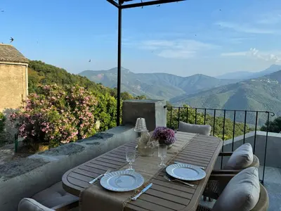 a table with plates and glasses on a balcony with mountains at Village House With Character In Corsica in Scolca