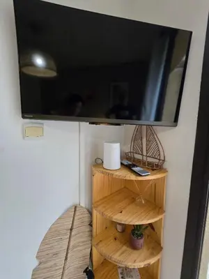 a flat screen tv on a wall with wooden shelves at Mini villa vue jardin dans résidence calme wifi piscine mer à pied in Serra-di-Ferro