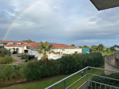 a rainbow over a house with a palm tree at Joli appartement résidentiel plage et piscine in Poggio-Mezzana