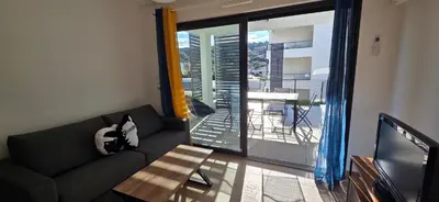 a living room with a black couch and a balcony at Joli T2 cozy, proche plages, Terra Doru B02 in Propriano