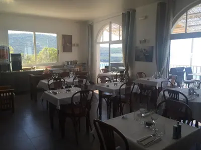 a dining room with tables and chairs and windows at Bel Mare in Cargèse