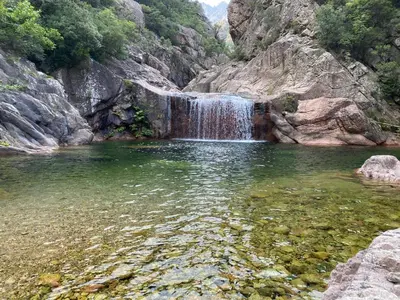 a waterfall in a pool of water next to a mountain at Pavillon au bord de la mer in Poggio-Mezzana