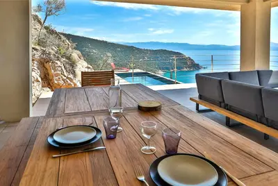 a wooden table with plates and wine glasses on a balcony at Villa petra mare in Cargèse