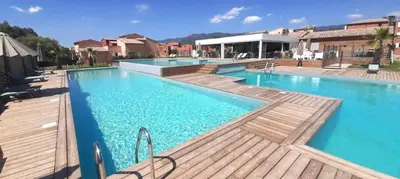 a large swimming pool with blue water and wooden decks at Résidence Luna, Saint-Cyprien in Porto-Vecchio