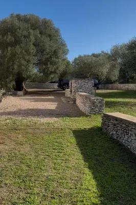 a stone wall in a field with a car in the background at Cozy mini villa proche plages, calme & activés in Bonifacio