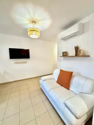 a living room with a white couch and a tv at Appartement 2 chambres - Rez-de-jardin - Avec piscine in Oletta