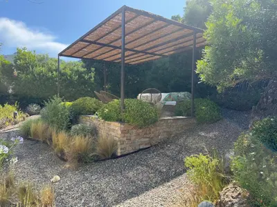 a stone wall with a wooden canopy in a garden at Villa Oletta, Saint Florent in Oletta