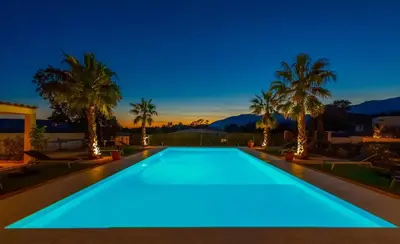 a swimming pool with blue lighting in a backyard with palm trees at Villa Suartello Porto Vecchio avec piscine privée in Porto-Vecchio