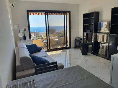 a living room with a couch and a view of the ocean at Le Balcon des Sanguinaires - studio cosy avec vue sur le Golfe d'Ajaccio et les Îles Sanguinaires in Ajaccio