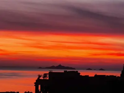 a sunset over the ocean with mountains in the background at Le Balcon des Sanguinaires - studio cosy avec vue sur le Golfe d'Ajaccio et les Îles Sanguinaires in Ajaccio