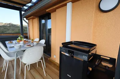 a grill on a deck with a table and chairs at L'Orizonte - T3 vue mer piscine et plage in Pianottoli-Caldarello