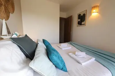 a white bed with blue pillows on top of it at L'Orizonte - T3 vue mer piscine et plage in Pianottoli-Caldarello