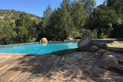 a swimming pool with rocks and trees in the background at Charming villa # Petra's House in Palombaggia in Porto-Vecchio