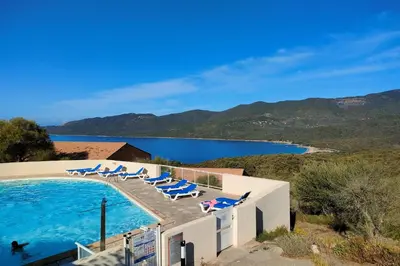 a swimming pool with lounge chairs and a body of water at Mini villa vue jardin dans résidence calme wifi piscine mer à pied in Serra-di-Ferro