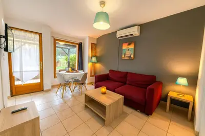 a living room with a red couch and a table at Mini villa vue jardin dans résidence calme wifi piscine mer à pied in Serra-di-Ferro