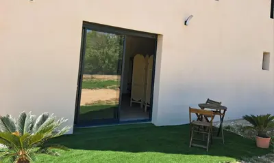 a room with a door and a chair on the grass at Lumineux studio entre terre et mer à 2min de la plage in Calcatoggio