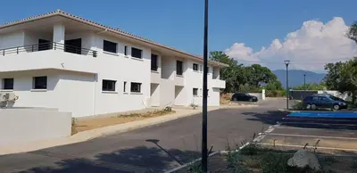 a white building with a car parked in a parking lot at Godichard Apartment in a residence for 46 people with swimming pool and in Porto-Vecchio