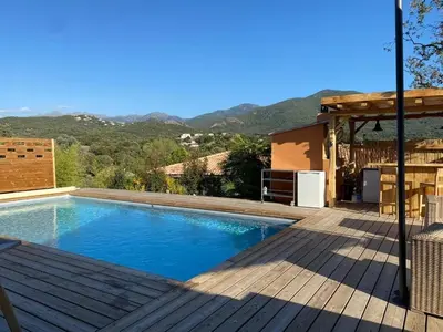 a swimming pool with a wooden deck and mountains in the background at Cozy villa with pool in Eccica-Suarella