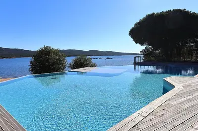 a large swimming pool next to a body of water at A Marinca - Plage privée et piscine chauffée in Pianottoli-Caldarello