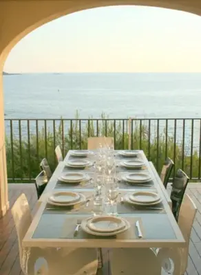 a table with plates and wine glasses on top of the ocean at Appartement les pieds dans l'eau in Calcatoggio