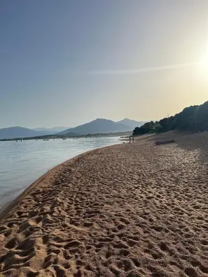 a sandy beach with people walking on it next to the water at Appartement T2 jardin & accès plage privée in Grosseto-Prugna