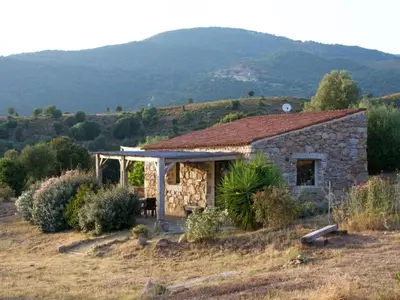 a stone house in a field with mountains in the background at Holiday Home in idyllischer Lage im Süden Korsikas by Interhome in Serra-di-Ferro