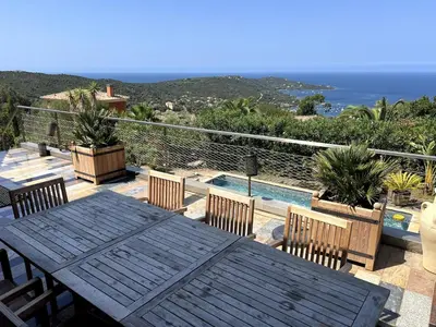 a patio with a wooden table and chairs and a pool at Villa Pierretti - Vue mer Panoramique in Coti-Chiavari