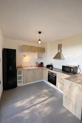 a kitchen with wooden cabinets and a black refrigerator at L'Immortelle - T3 avec balcon vue mer & montagne in Calenzana