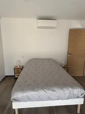 a bed in a room with a white wall at Rez de villa Proche d'Ajaccio in Sarrola-Carcopino