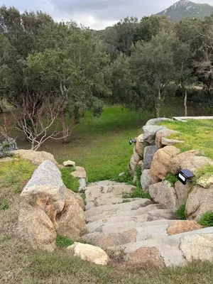 a stone path in a field with rocks and trees at Maison de campagne in Sartène