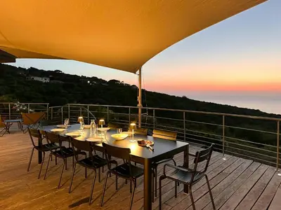 a dining table on a deck with a view of the ocean at Villa On One Hectare Facing The Gulf Of Ajaccio in Coti-Chiavari