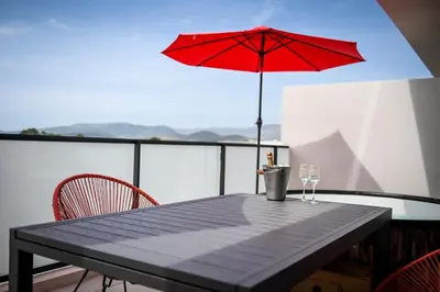 a table with a red umbrella and two wine glasses at Résidence Porticcio Vacations Vue Mer Piscine & Jacuzzi in Grosseto-Prugna