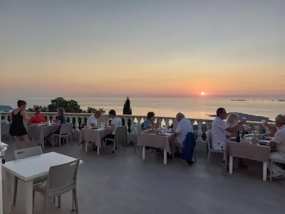 a group of people sitting at tables on a patio with the sunset at le Belvedere in Coti-Chiavari