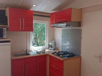 a kitchen with red cabinets and a sink and a window at Mobil home 6 personnes avec terrasse à Vico - API-1-52-841 in Vico