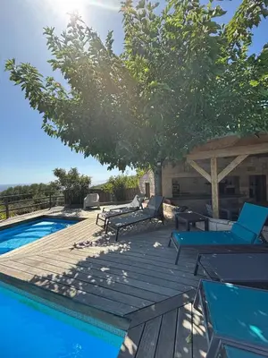 a swimming pool with a wooden deck next to a tree at VILLA Cala D'orzu in Coti-Chiavari