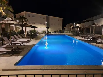 a swimming pool at night with chairs and umbrellas at Petit havre de paix au bord de la mer in Linguizzetta