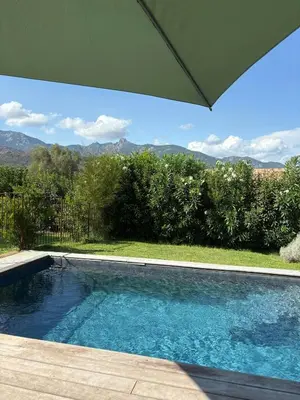 a swimming pool with an umbrella and mountains in the background at Stone House Between Porto-Vecchio And Bonifacio in Figari