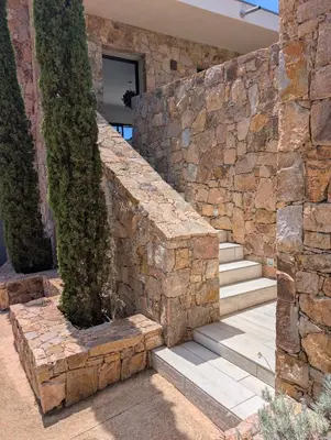 a stone wall with stairs and trees in front of a house at Villa Luxueuse avec piscine privee chauffee in Porto-Vecchio