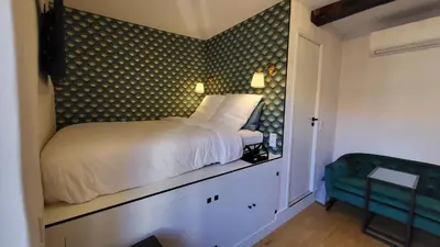 a small bedroom with a bed and a green chair at Studio de charme Cœur d'Ajaccio in Ajaccio