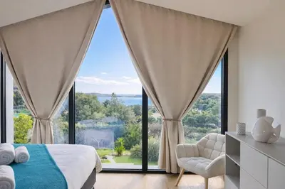 a bedroom with large windows and a bed and a chair at Villa di Stella Pinarello - Proche plage - swimming pools in Sainte-Lucie de Porto-Vecchio